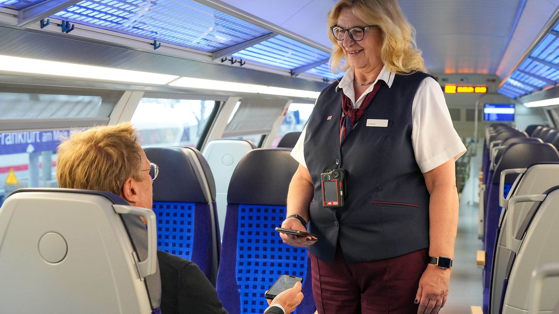 Eine Kundenbetreuer:in von DB Regio kontrolliert einen Reisenden und trägt dabei eine Bodycam.