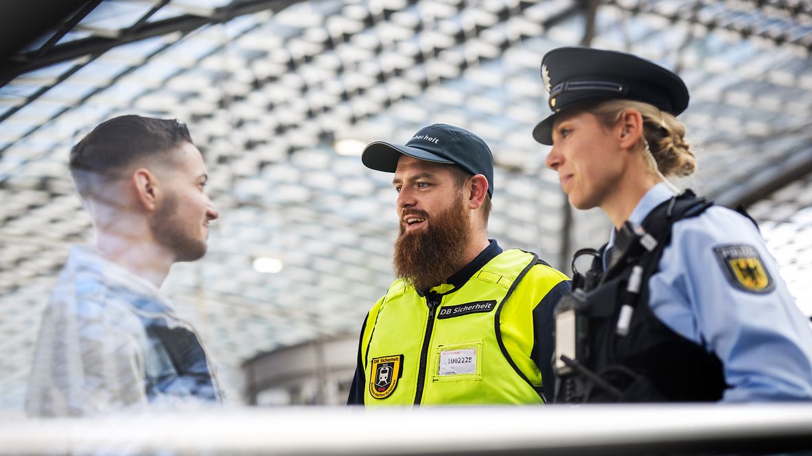 Eine Bundespolizistin und Mitarbeitender von DB Sicherheit im Gespräch mit einem Reisenden