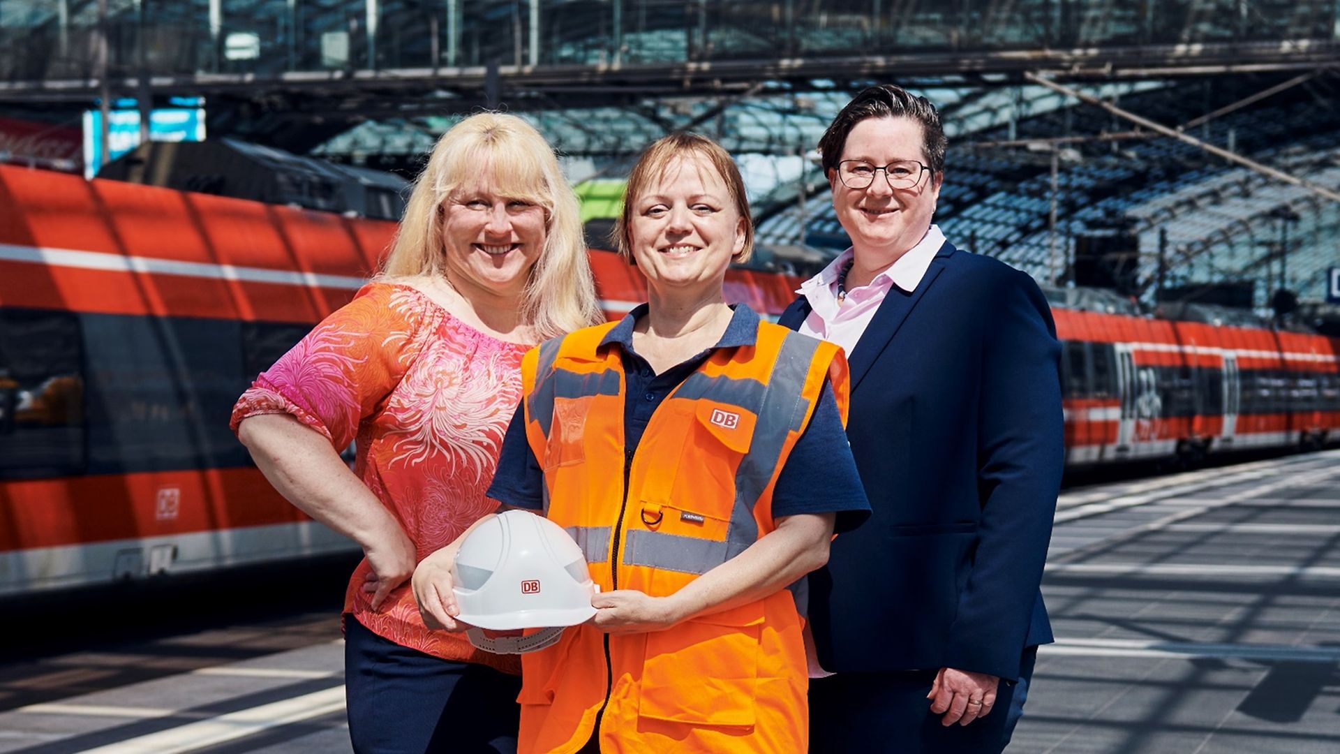 Drei Deutsche-Bahn-Mitarbeiterinnen aus verschiedenen Berufsfeldern stehen gemeinsam auf dem Gleis.