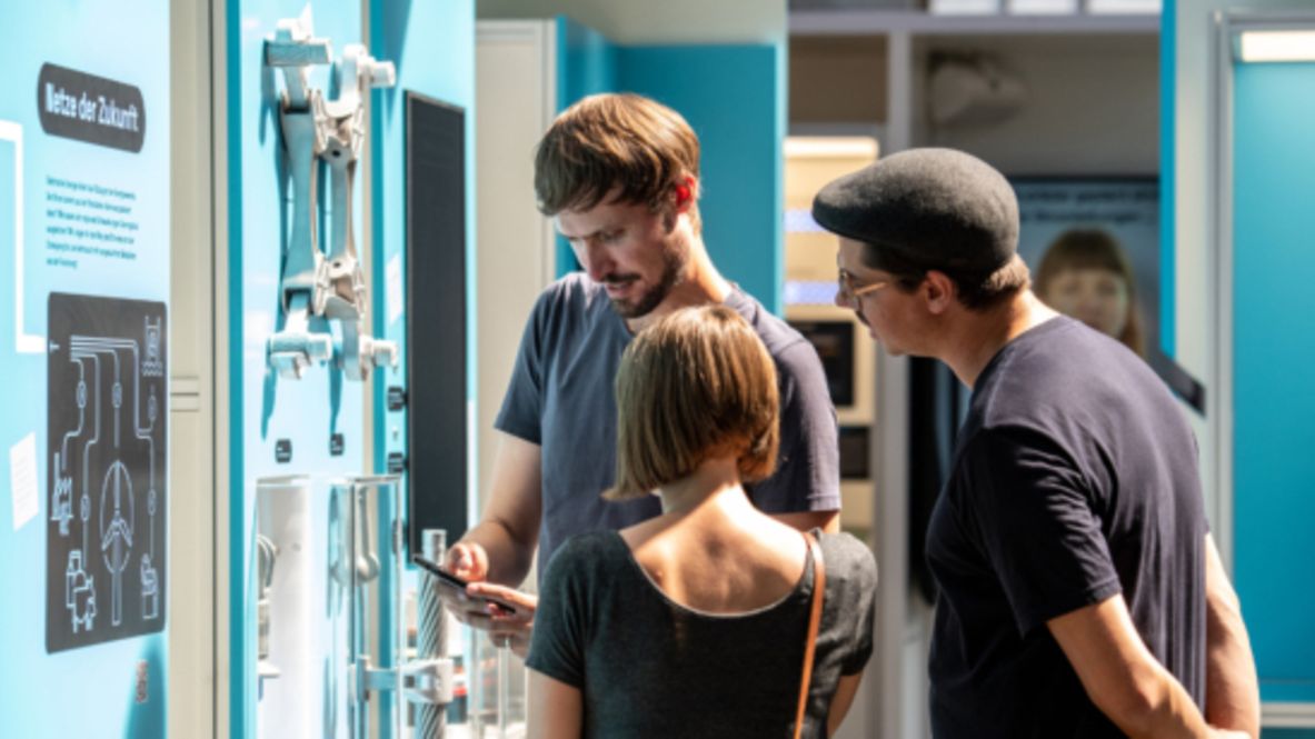Drei Personen stehen vor einer blauen Themenwand mit Informationen.