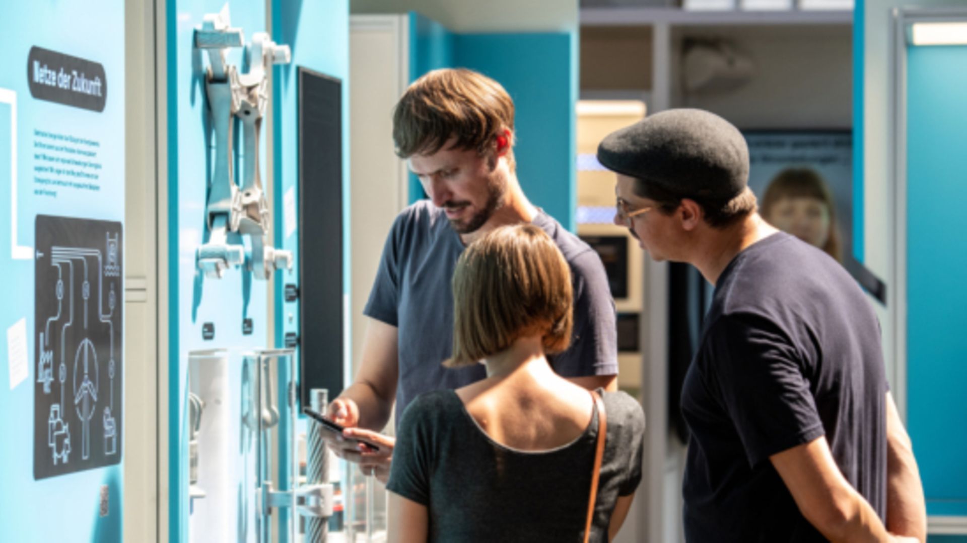 Drei Personen stehen vor einer blauen Themenwand mit Informationen.