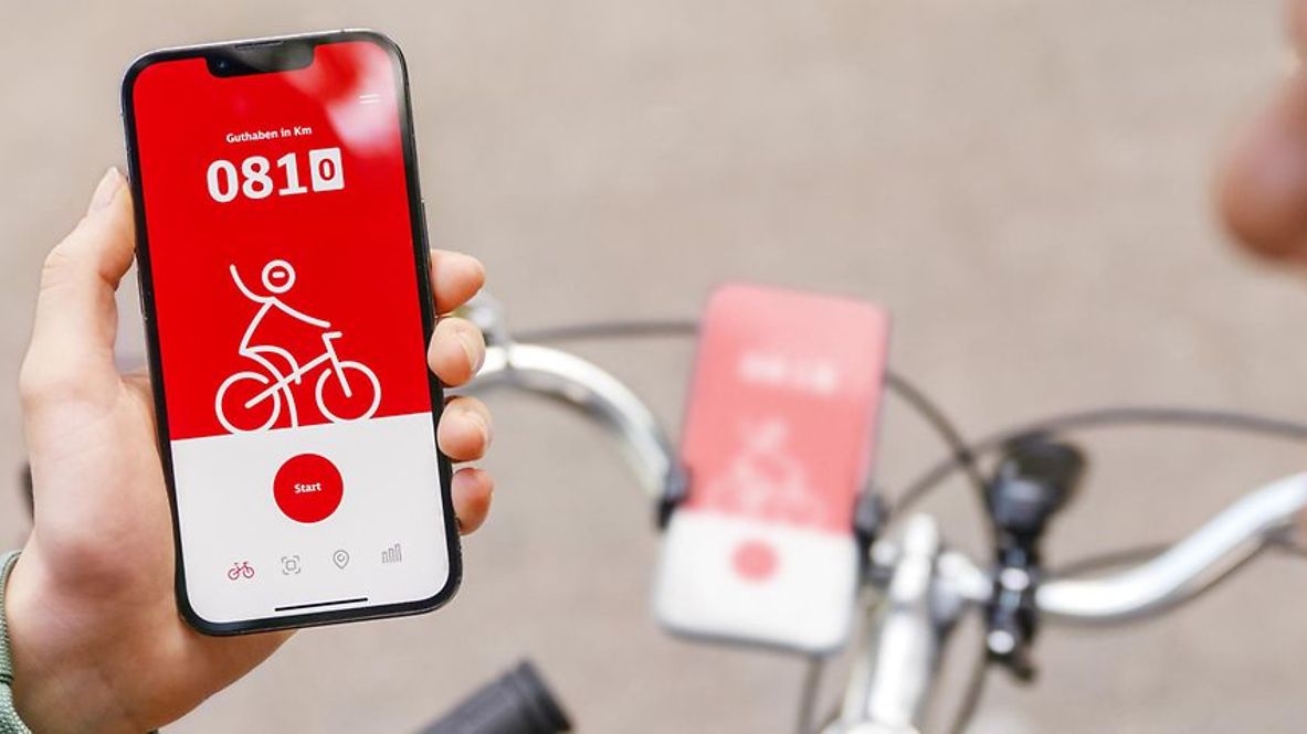 Zwei Radfahrende schauen auf ein Handy, auf dem die DB Rad+ App angezeigt wird.