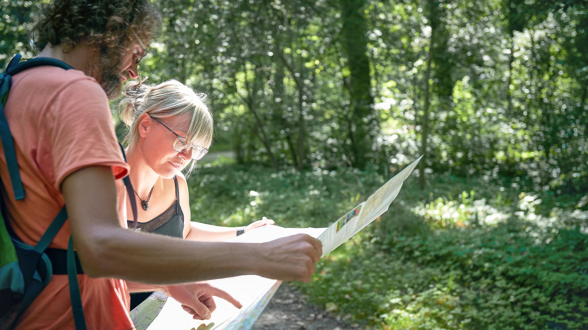 A man and a woman are standing in the forest looking at a map and orienting themselves on a hike.