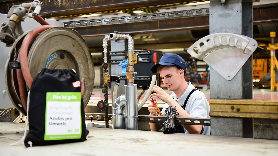 Trainee working on cables in the workshop. In the foreground, a DB cloth bag with Das ist grün. print.