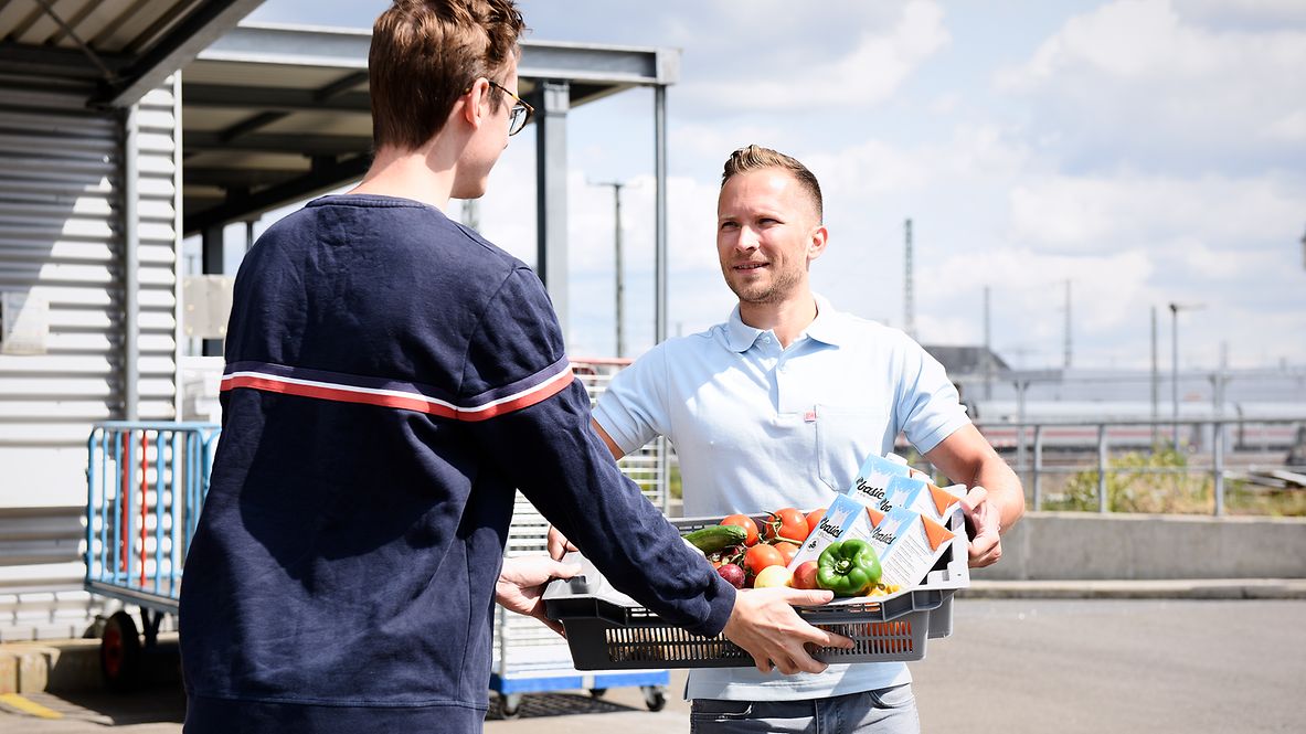 A DB employee hands over a basket of food donations to a food bank employee. 
