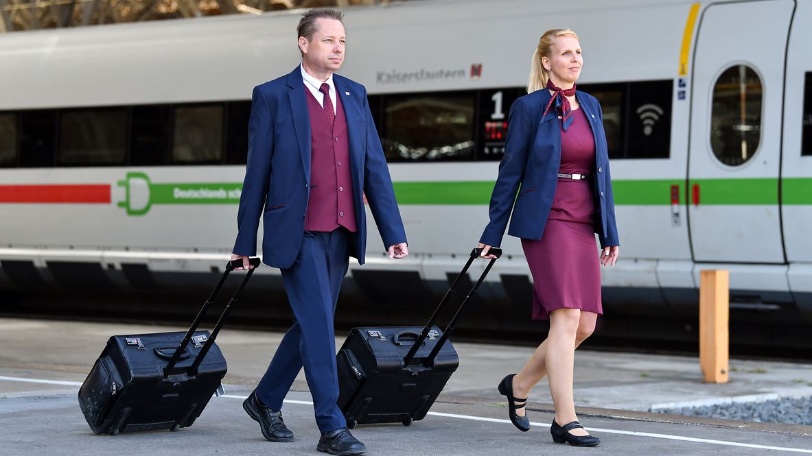 Two members of the train crew is walking along the platform wearing DB corporate clothing.