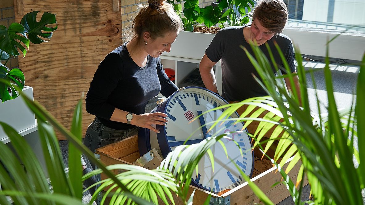 Two employees in an office put a station clock in a box.