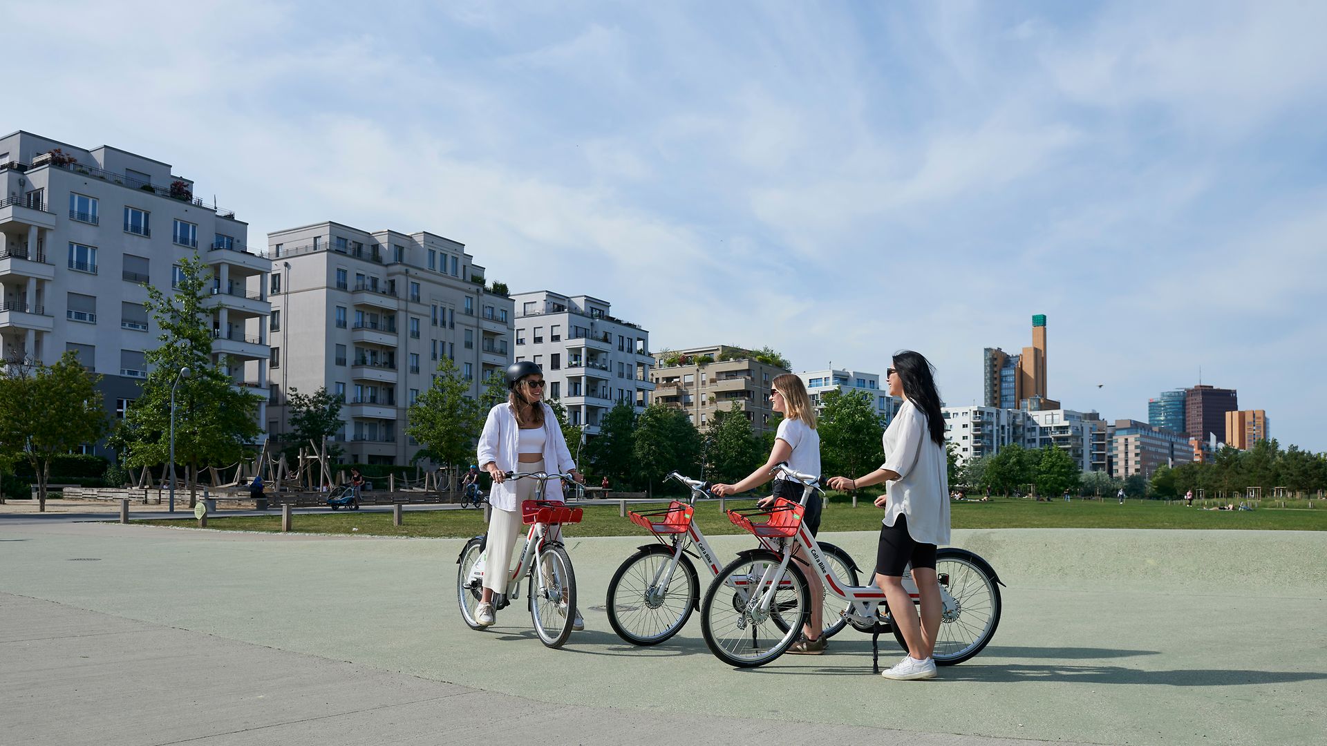 Three women greet each other in a park, each with a bike from the Call a Bike initiative.