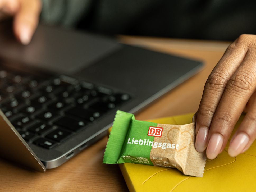 The hand of a woman holding a chocolate next to a laptop.