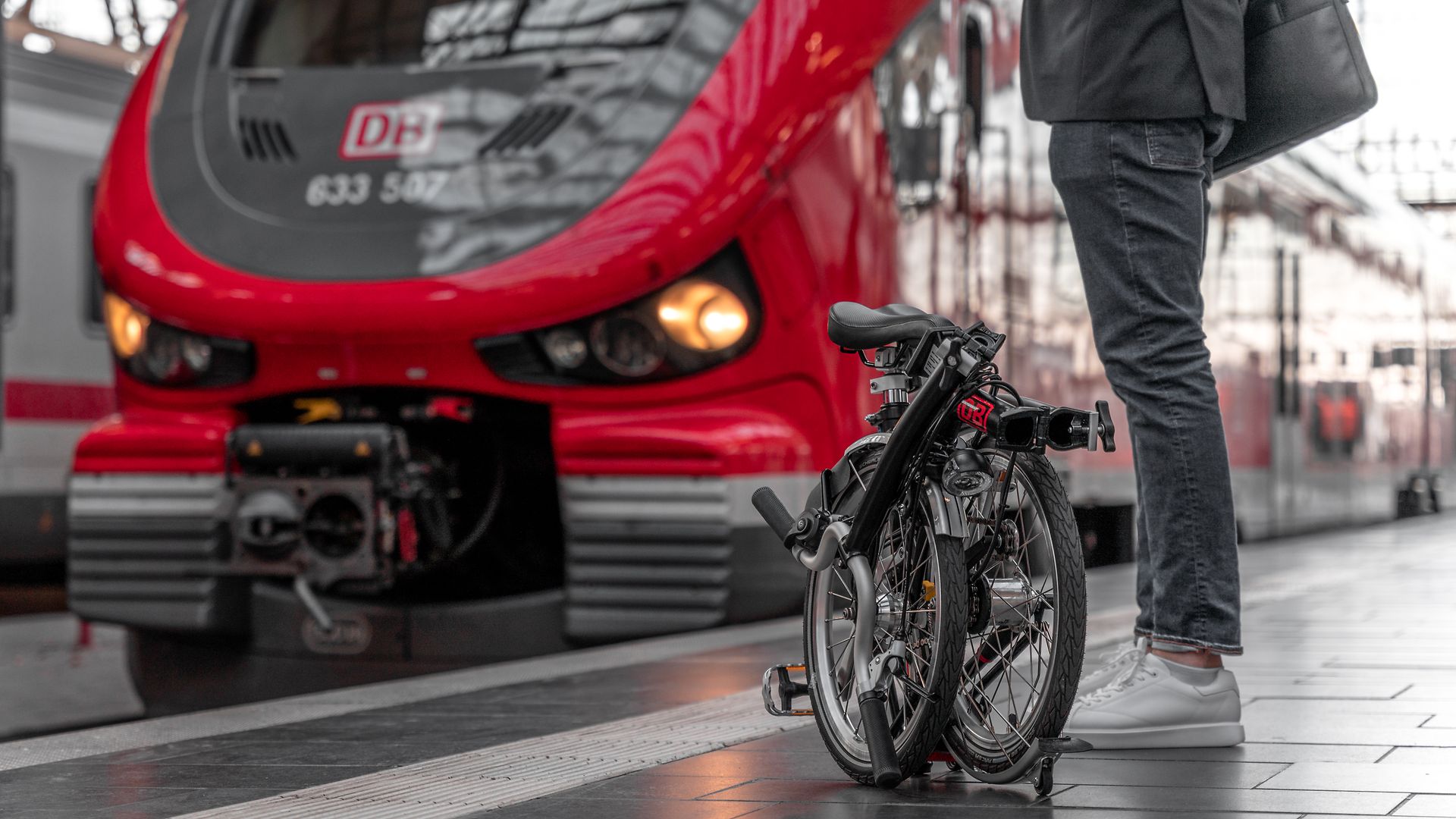 A man is standing in front of an ICE train with a folded folding bike.