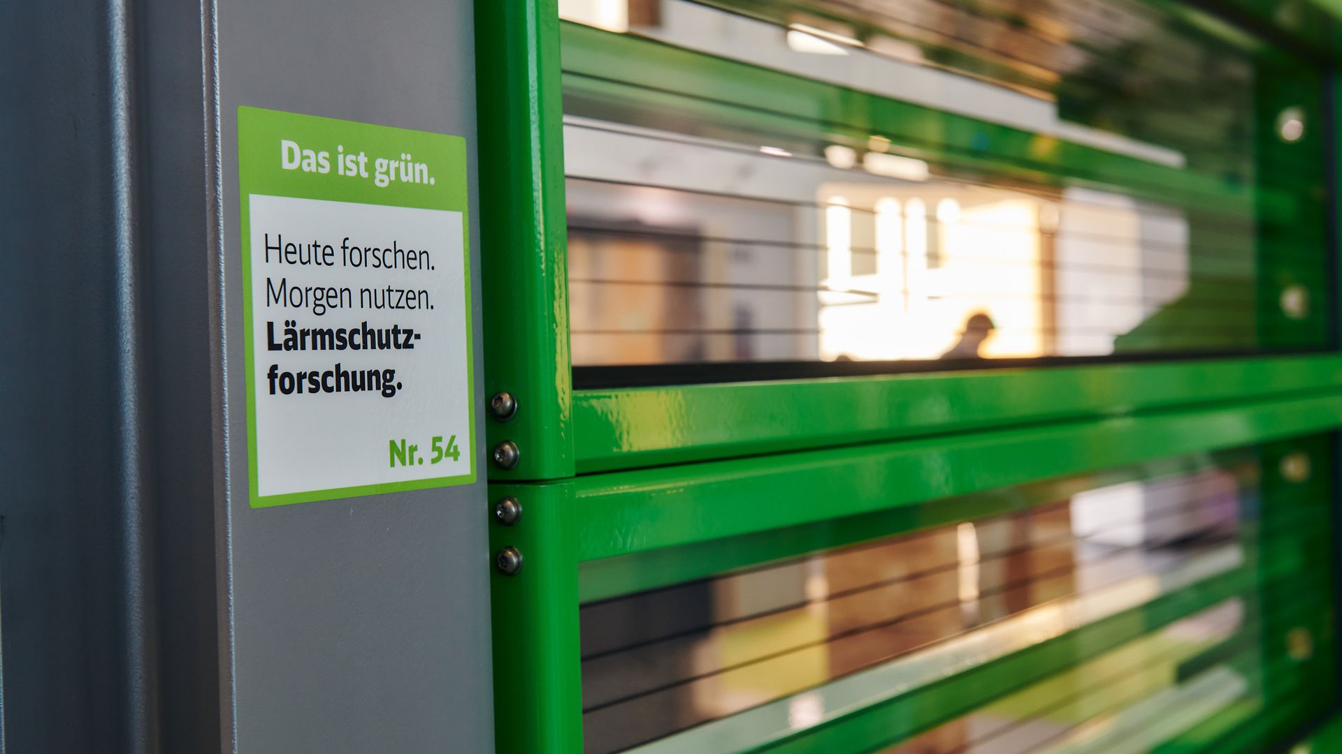 Transparent elements of a noise barrier with a green frame and a sticker of the DB environmental brand Das ist grün.