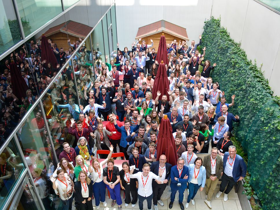 A group of young vocational trainees stand in the courtyard of a building and raise their hands in jubilation.