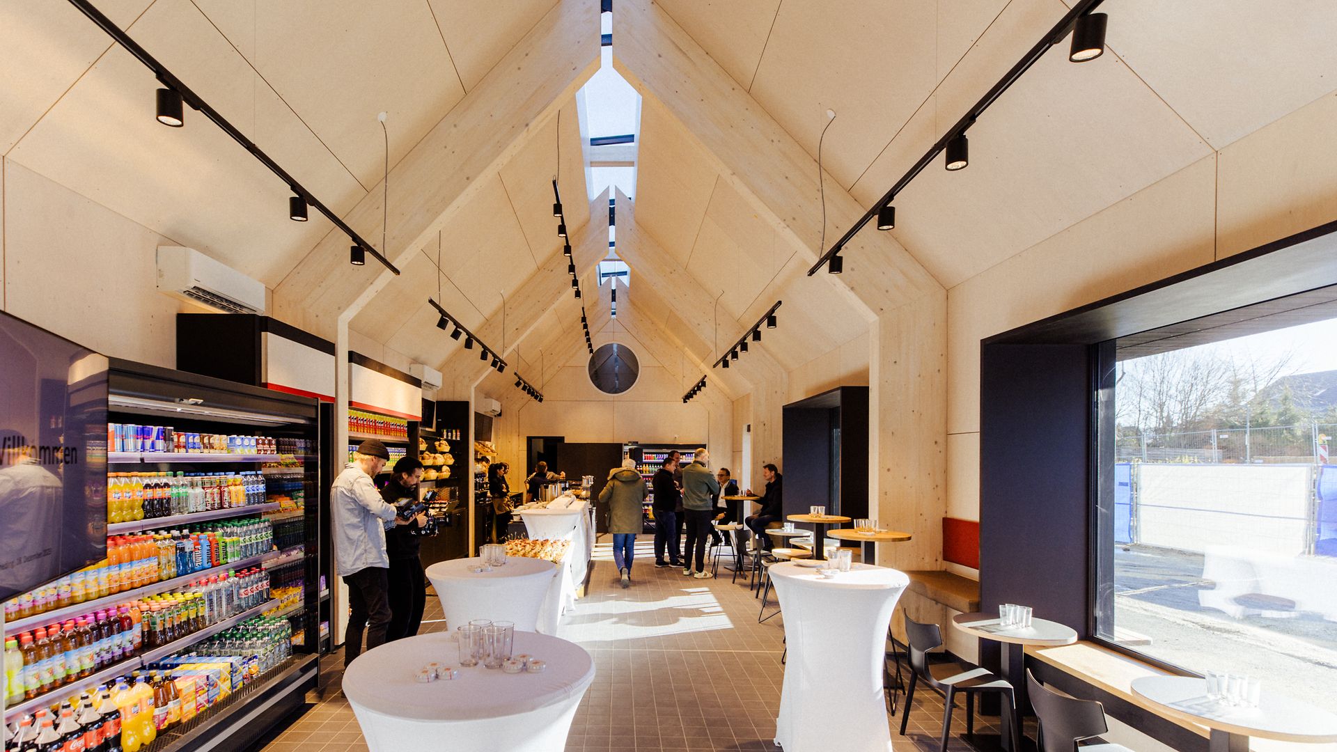 View of the reception building in Zorneding with shelves, bar tables and people in the background