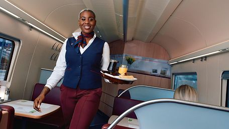 A DB employee carries a tray of food on a train. 