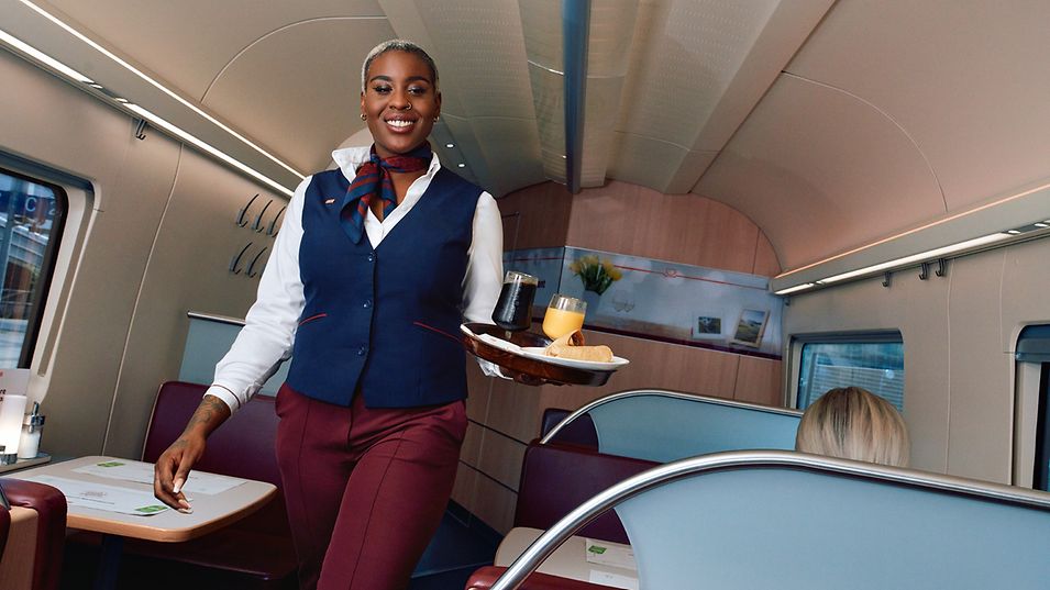 A DB employee carries a tray of food on a train. 