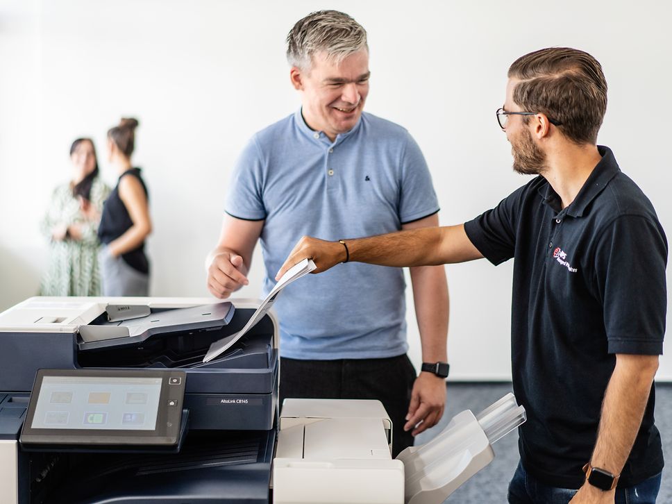 Two office workers are chatting by the printer.