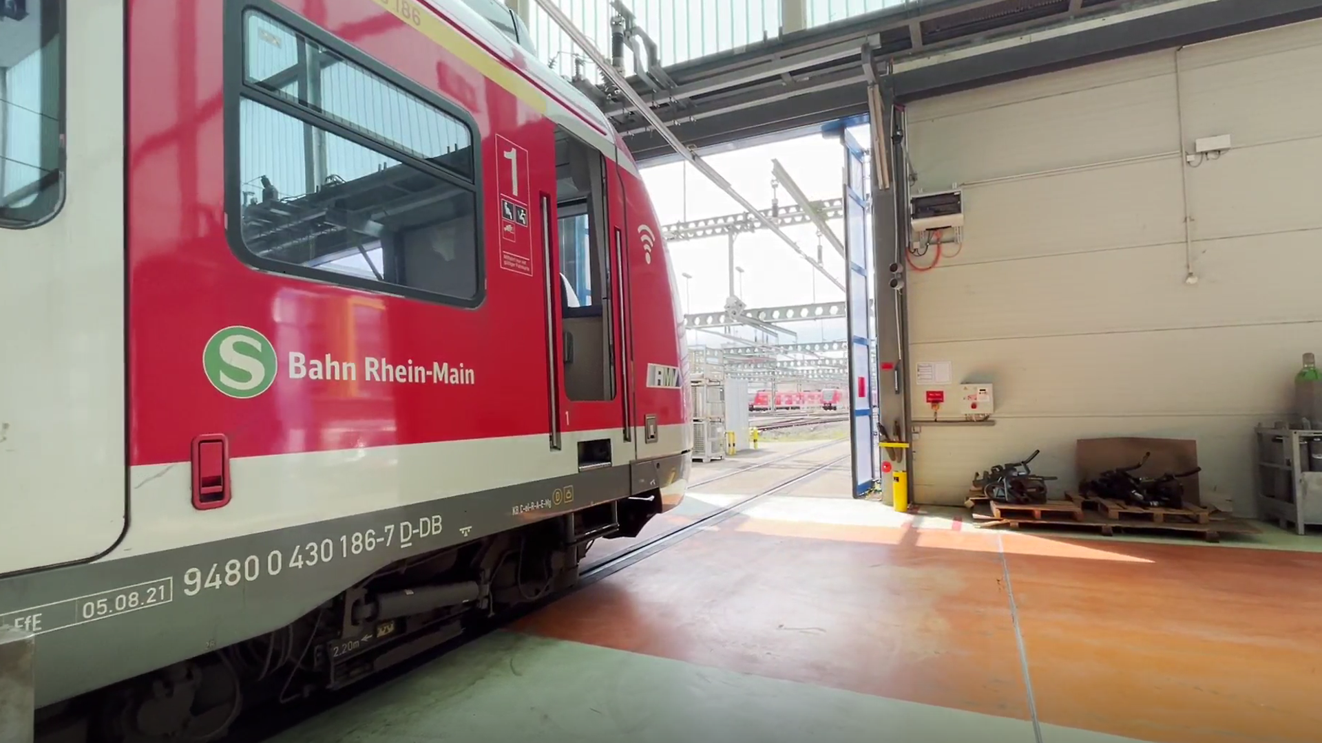 A red train stands on tracks in the hall of a maintenance depot, the hall doors close behind it.