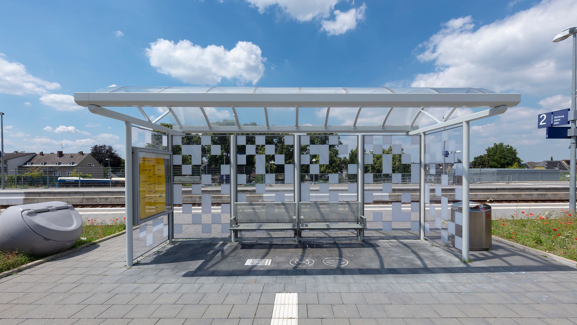 A glass bus shelter with benches on the platform under a blue sky