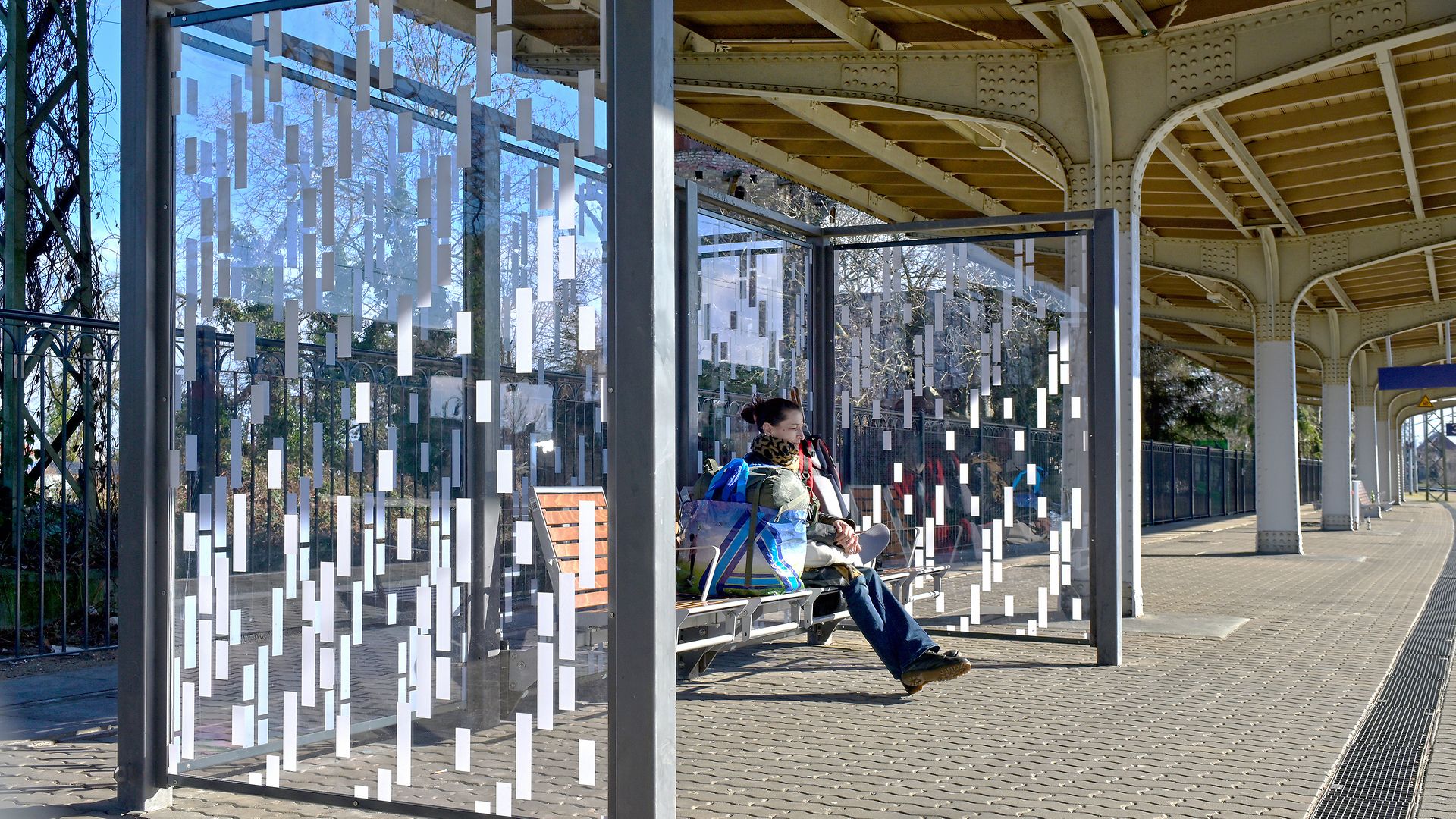 A glass bus shelter with geometric patterns on the walls, a person sitting on a bench.