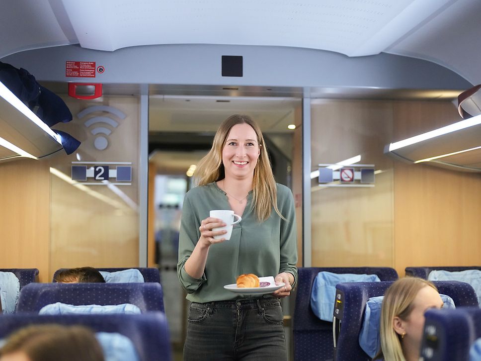 Passenger walks through the train carrying porcelain dishes in her hand.