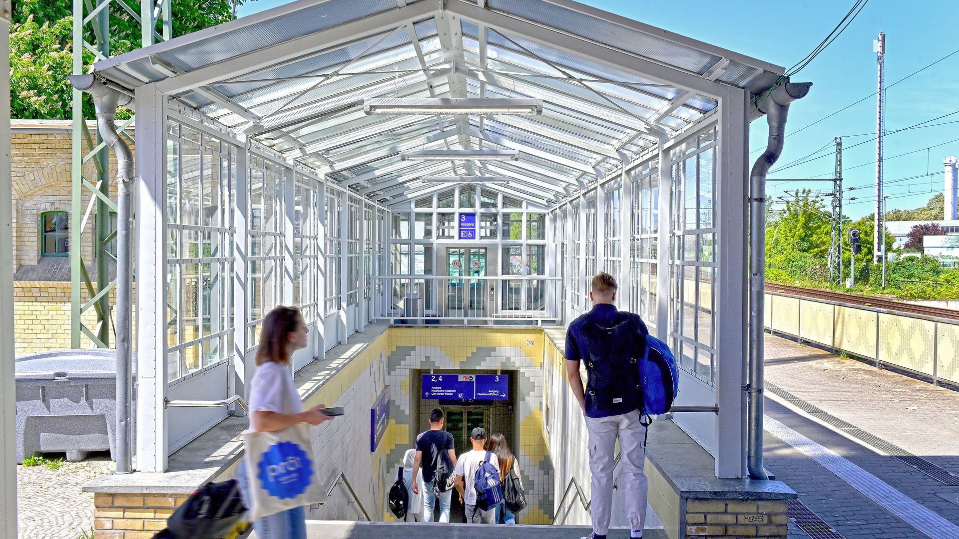 The entrance to a pedestrian subway with a glass roof, several people walking down the stairs.
