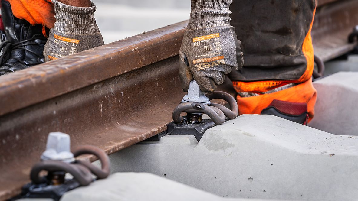 A track construction worker installs bolts on a section of rail.