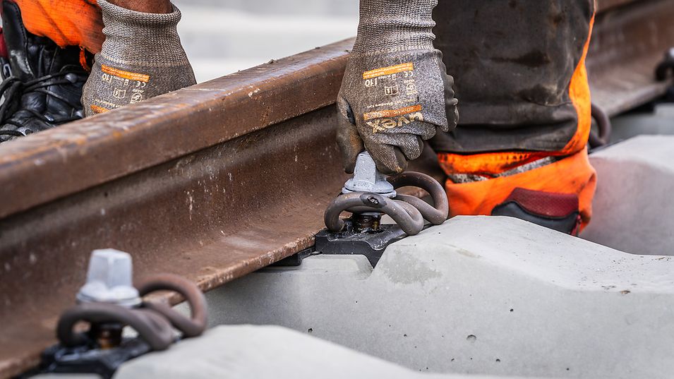 A track construction worker installs bolts on a section of rail.